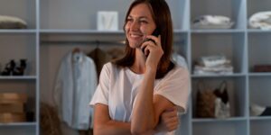 Mulher sorridente atendendo cliente por telefone em loja de roupas e acessórios