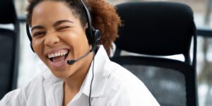 Atendente sorridente com headset piscando enquanto realiza atendimento ao cliente