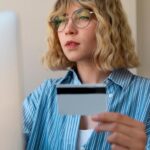 Mulher jovem segurando cartão de crédito enquanto realiza compra online no computador