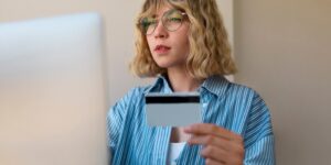Mulher jovem segurando cartão de crédito enquanto realiza compra online no computador