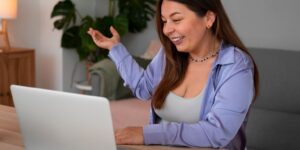 Mulher sorridente interagindo em chamada de vídeo pelo laptop em ambiente doméstico