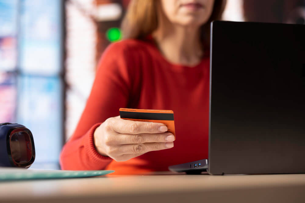 Mulher realizando compra online com cartão de crédito em frente ao notebook