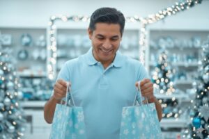 Homem sorrindo segurando sacolas de compras em loja decorada para o Natal