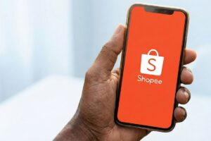 Mão segurando smartphone com a tela inicial da Shopee aberta, representando vendas online e passo a passo para se tornar vendedor indicado.