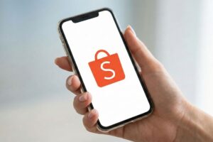 Mão segurando smartphone com o ícone da Shopee na tela, representando vendas online e importância do selo de vendedor indicado.