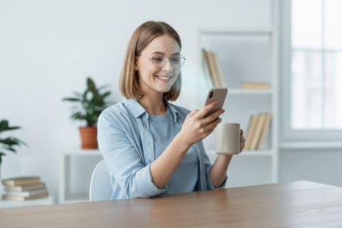 Mulher sorridente usando reconhecimento facial no celular enquanto toma café