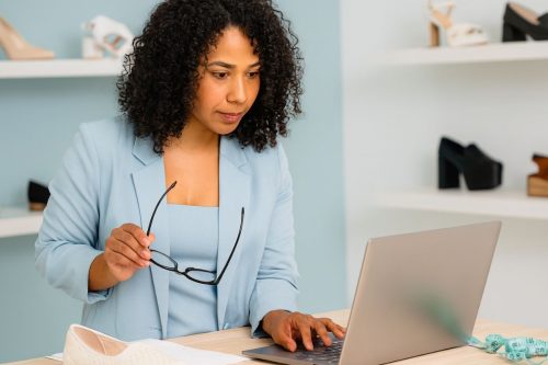 Mulher empreendedora analisando vendas no notebook em loja de calçados