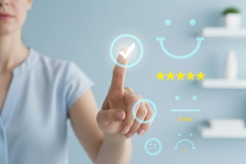 Pessoa tocando ícone digital de avaliação com cinco estrelas e símbolo de sorriso, representando satisfação do cliente e excelência no atendimento.