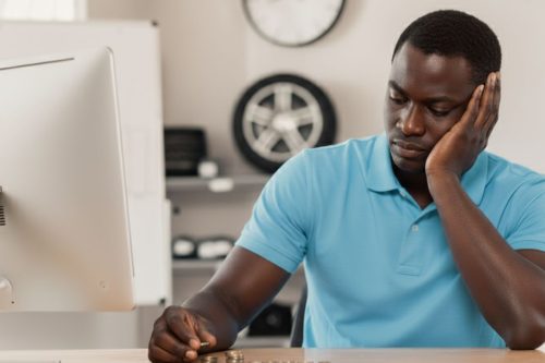 Homem preocupado contando moedas em frente ao computador representando queda nas vendas