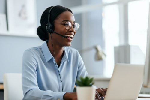 Mulher atendendo cliente com fone de ouvido e microfone enquanto usa notebook em escritório