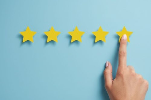 Mão avaliando com cinco estrelas em fundo azul simbolizando reputação positiva