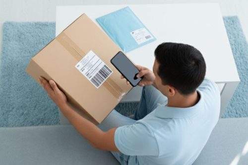 Homem escaneando código de barras em caixa de encomenda com celular