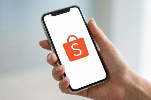 Mão segurando smartphone com o ícone da Shopee na tela, representando vendas online e importância do selo de vendedor indicado.
